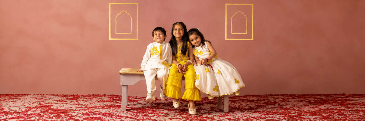 Three children in traditional festive outfits sitting on a bench